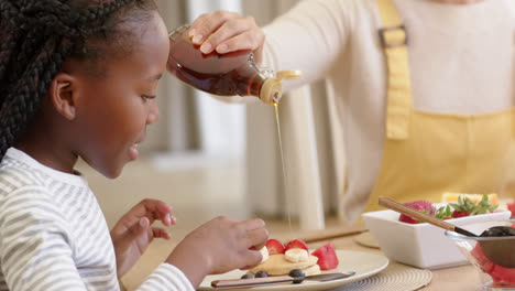 Glückliche-Afroamerikanische-Mutter-Und-Tochter-Essen-Pfannkuchen-Zu-Hause,-Zeitlupe