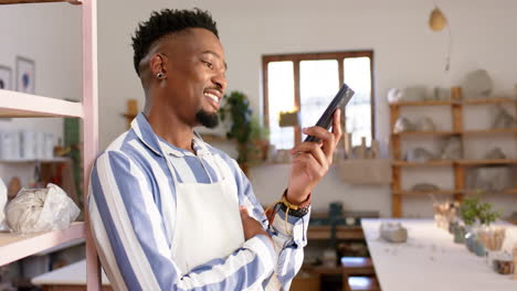 Glücklicher-Afroamerikanischer-Mann-Mit-Bart,-Der-Am-Telefon-Spricht-Und-Im-Töpferstudio-Lächelt,-Zeitlupe