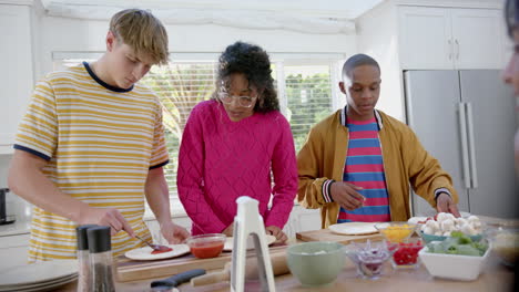 Happy-diverse-group-of-teenage-friends-cooking-and-making-pizza-in-kitchen,-slow-motion