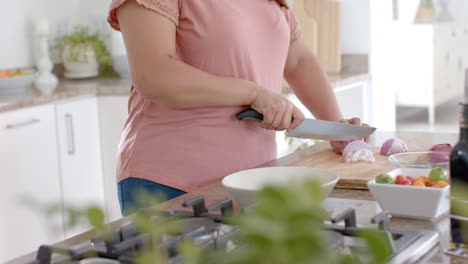 Happy-plus-size-biracial-woman-chopping-vegetables-in-kitchen-at-home,-slow-motion