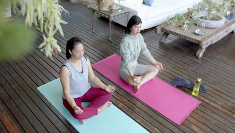 Focused-asian-female-friends-practicing-yoga-meditation-on-sunny-terrace,-slow-motion