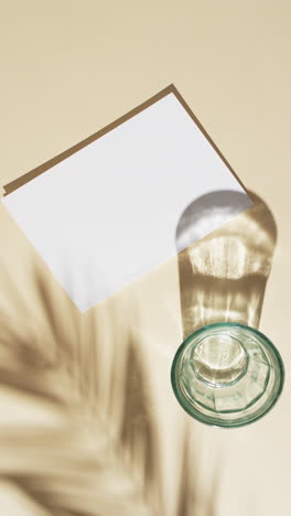 Vertical-video-of-glass-and-book-with-white-blank-pages-with-copy-space-on-white-background