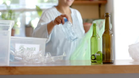 Happy-senior-biracial-woman-segregating-plastic-bottles-at-home,-slow-motion