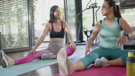 Happy-asian-female-friends-stretching-and-smiling-in-sunny-home-gym,-slow-motion