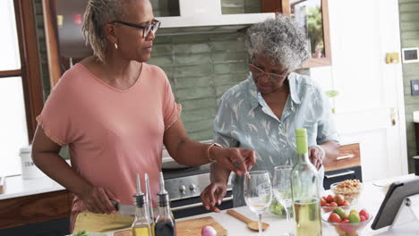 Senior-african-american-female-friends-cooking,-preparing-vegetables-and-using-tablet,-slow-motion