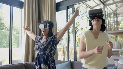 Happy-asian-female-friends-using-vr-glasses-and-dancing-in-sunny-living-room,-slow-motion