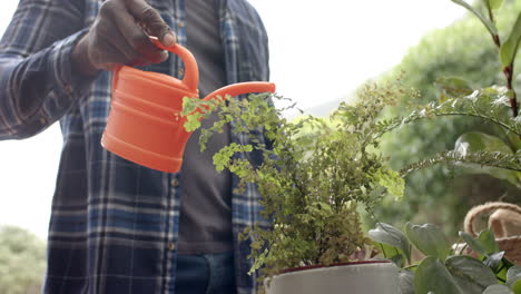 Midsection-of-mature-african-american-man-watering-plants-in-garden,-slow-motion