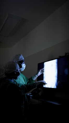 Vertical-video-of-diverse-surgeons-discussing-with-x-ray-scans-in-operating-theatre,-slow-motion