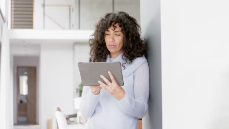 Happy-mature-caucasian-woman-leaning-on-wall-using-tablet-at-home,-slow-motion