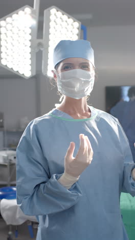 Vertical-video-of-portrait-of-caucasian-female-surgeon-in-operating-theatre,-slow-motion