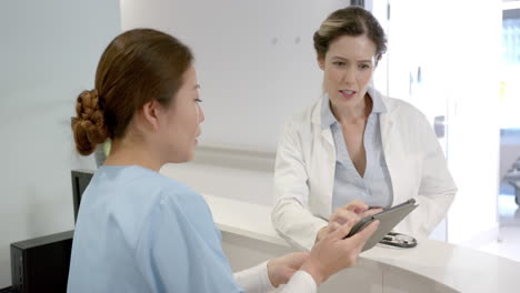 Se-Centró-En-Diversas-Doctoras-Usando-Tabletas-Y-Discutiendo-Sobre-El-Mostrador-De-Recepción-Del-Hospital,-En-Cámara-Lenta