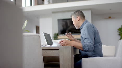 Senior-biracial-man-using-smartphone-and-laptop-at-desk,-working-from-home,-copy-space,-slow-motion