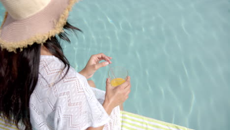 Biracial-teenage-girl-in-sunhat-drinking-juice-by-pool,-copy-space,-slow-motion