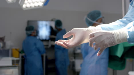 Midsection-of-african-american-surgeon-wearing-surgical-gloves-in-operating-theatre,-slow-motion