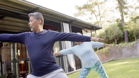 Focused-diverse-senior-couple-practicing-yoga-in-garden