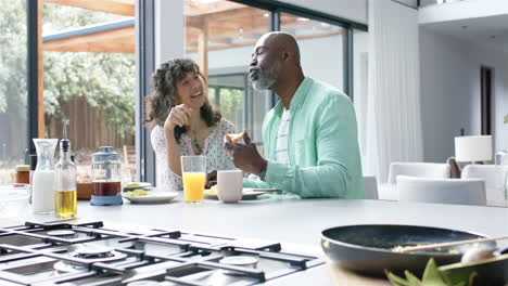 Happy-biracial-couple-having-breakfast-and-talking-in-kitchen,-slow-motion