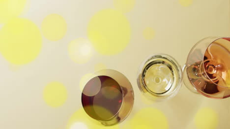 Composite-of-glasses-of-white,-rose-and-red-wine-over-yellow-spots-on-yellow-background
