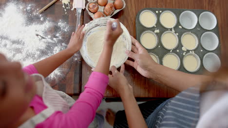 Overhead-of-biracial-mother-and-daughter-baking,-mixing-cake-mix,-slow-motion