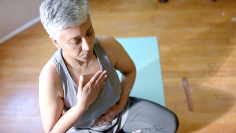 Focused-senior-biracial-woman-meditating-on-yoga-mat-at-home