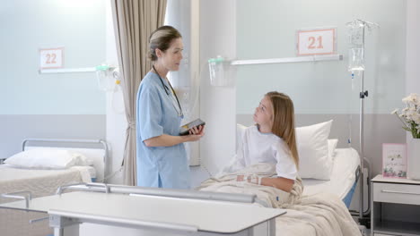 Caucasian-female-doctor-with-tablet-talking-with-girl-patient-in-hospital-bed,-slow-motion