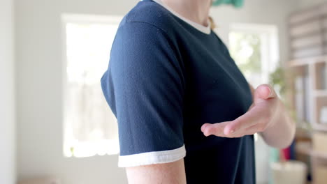Midsection-of-caucasian-woman-in-navy-blue-t-shirt-showing-white-edging-in-sunny-room,-slow-motion