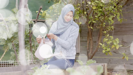Animation-of-spots-of-light-over-biracial-woman-in-hijab-with-watering-can,-gardening