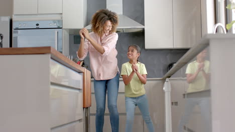 Happy-biracial-mother-and-daughter-having-fun-dancing-together-in-kitchen,-copy-space,-slow-motion