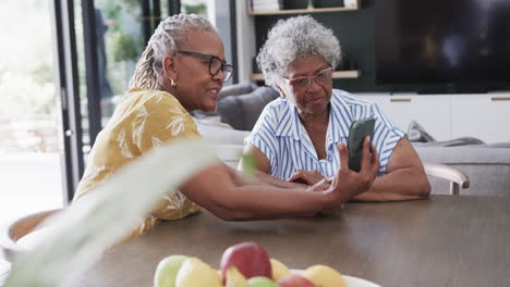 Senior-african-american-female-friends-using-smartphone-and-talking-in-dining-room,-slow-motion