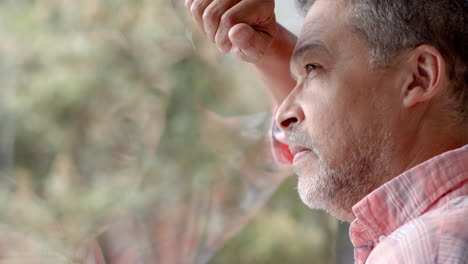 Thoughtful-senior-biracial-man-looking-out-of-window-at-countryside,-copy-space,-slow-motion