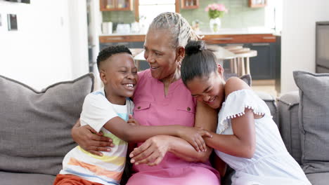 Happy-african-american-grandchildren-and-grandmother-embracing-on-sofa,-slow-motion