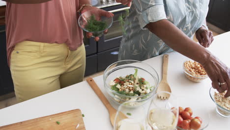 Midsection-of-senior-african-american-female-friends-preparing-salad-in-kitchen,-slow-motion