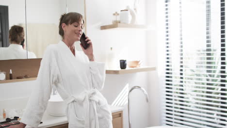 Caucasian-woman-in-a-white-robe-talks-on-the-phone,-smiling
