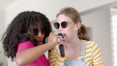 Happy-diverse-teenage-female-friends-dancing-and-singing-with-glasses-at-home,-slow-motion
