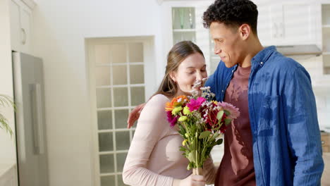 Happy-diverse-couple-holding-flowers-and-embracing-at-home,-in-slow-motion