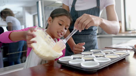 Happy-biracial-mother-and-daughter-pouring-cake-mix-into-cake-forms-in-kitchen,-slow-motion