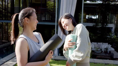 Happy-asian-female-friends-with-exercise-mats-laughing-on-sunny-terrace,-slow-motion