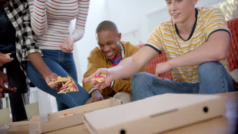 Fröhliche,-Vielfältige-Gruppe-Von-Teenager-Freunden,-Die-Auf-Der-Couch-Sitzen-Und-Zu-Hause-Pizza-Essen,-Zeitlupe