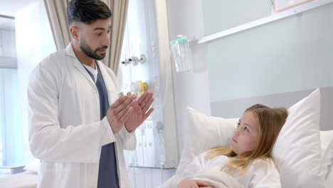 Diverse-male-doctor-with-asthma-inhaler-explaining-to-girl-patient-in-hospital-bed,-slow-motion