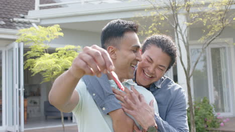 Portrait-of-happy-diverse-gay-male-couple-with-new-house-keys-embracing-in-garden,-slow-motion