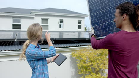 Busy-diverse-couple-using-tablet-with-copy-space-and-carrying-solar-panel-in-garden,-slow-motion