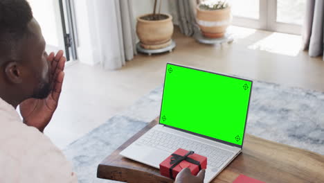 African-american-man-holding-red-gift-and-using-laptop-with-copy-space-on-green-screen