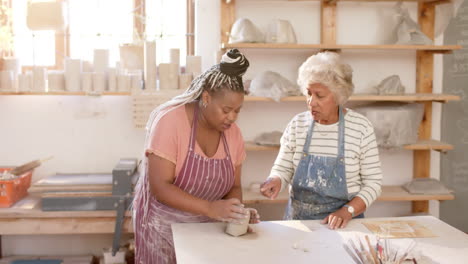 Two-diverse-female-potters-working-on-clay-vase-and-discussing-in-pottery-studio,-slow-motion