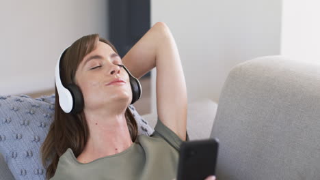 Caucasian-woman-enjoys-music-with-closed-eyes,-wearing-white-headphones