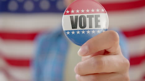 Hand-of-biracial-teenage-girl-agaisnt-american-flag-holding-vote-badge,-slow-motion