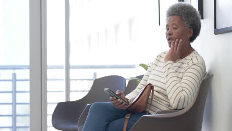 African-american-senior-woman-using-smartphone-in-hospital-waiting-room,-slow-motion