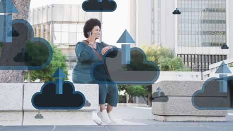 Animation-of-cloud-and-arrow-icons-over-african-american-woman-using-smartphone-in-city