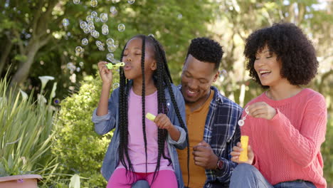 Happy-african-american-parents-with-daughter-blowing-bubbles-in-garden-at-home,-slow-motion