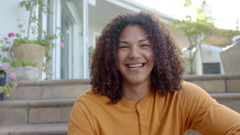 Portrait-of-happy-biracial-man-with-long-curly-hair-smiling-in-sunny-garden,-slow-motion