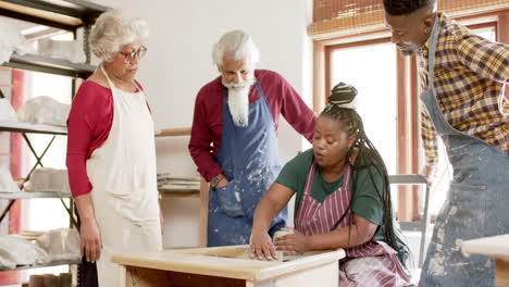 Happy-african-american-female-potter-and-others,-using-potter's-wheel-in-pottery-studio,-slow-motion