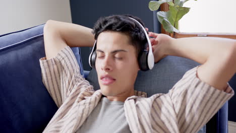 Happy-biracial-man-wearing-headphones-lying-on-couch-relaxing,-slow-motion